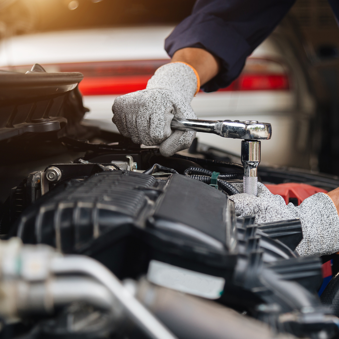 man using a tool to do work on his engine - he is wearing a mechanic outfit and oil gloves