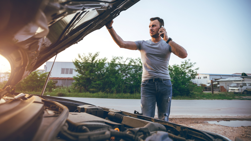 Man standing with his car bonnet open on the phone 