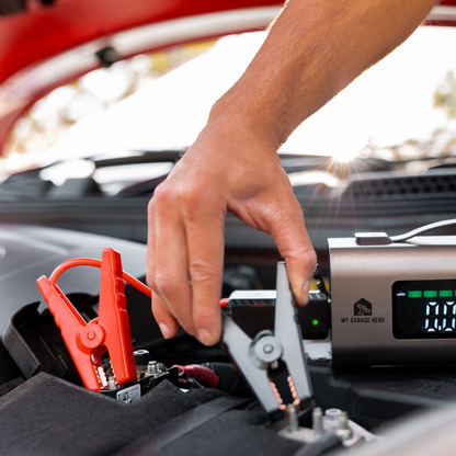 Close-up of a person connecting the Boost N’ Inflate jump-starter clamps to a vehicle battery, with the unit powered on beside the engine bay during a real jump-start setup.