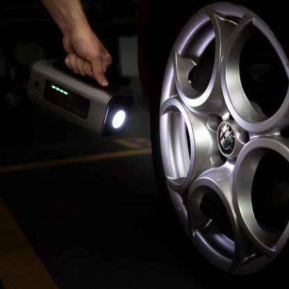 Person holding the Boost N’ Inflate with its LED torch switched on, illuminating an Alfa Romeo alloy wheel inside a dimly lit garage.