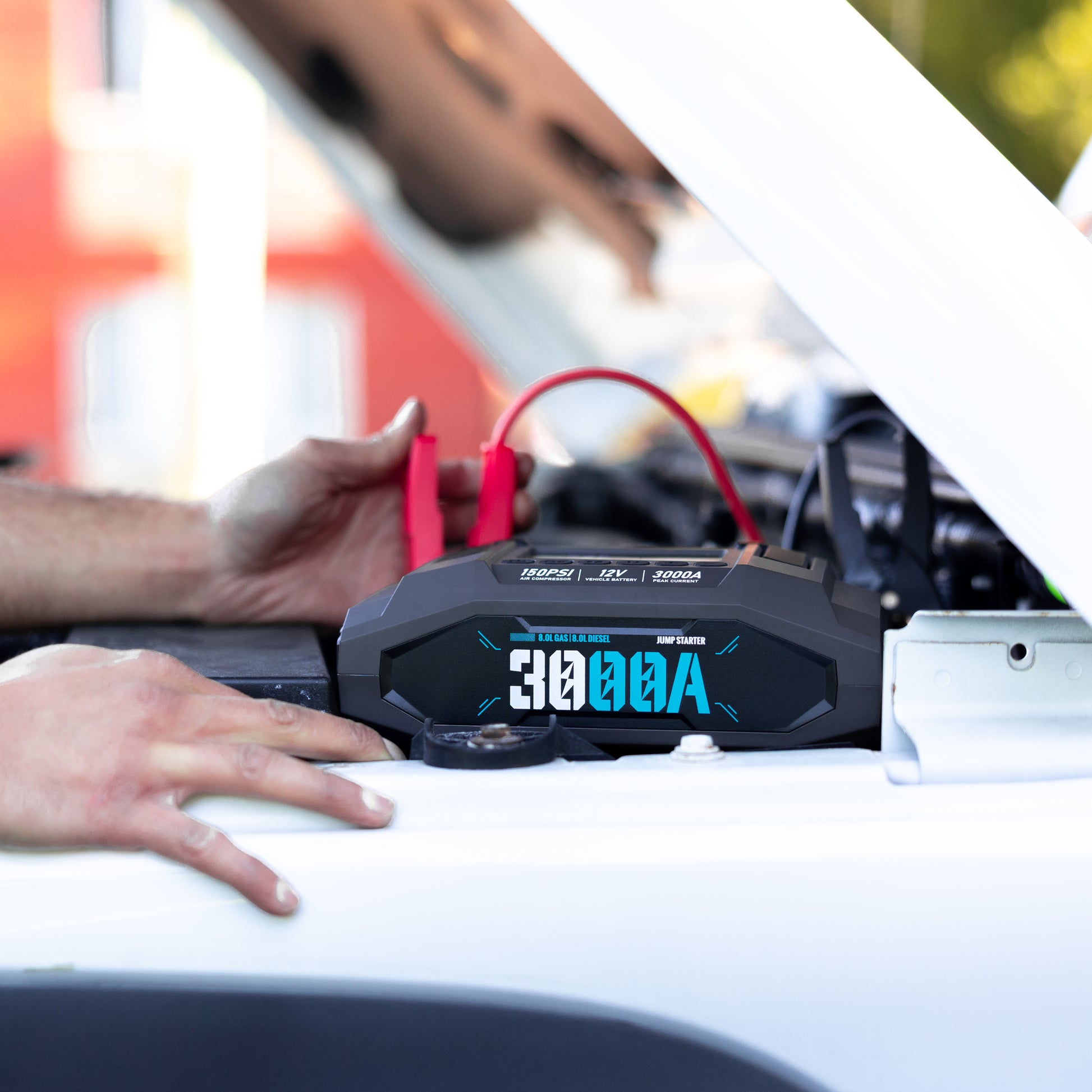 Boost N’ Inflate Pro positioned on the engine bay while a person connects the jump-start clamps, showing real-world use during a vehicle jump-start.