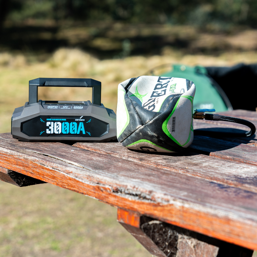 Boost N’ Inflate Pro placed on an outdoor timber table beside a partially deflated football, showing its ability to inflate sports balls during outdoor use.