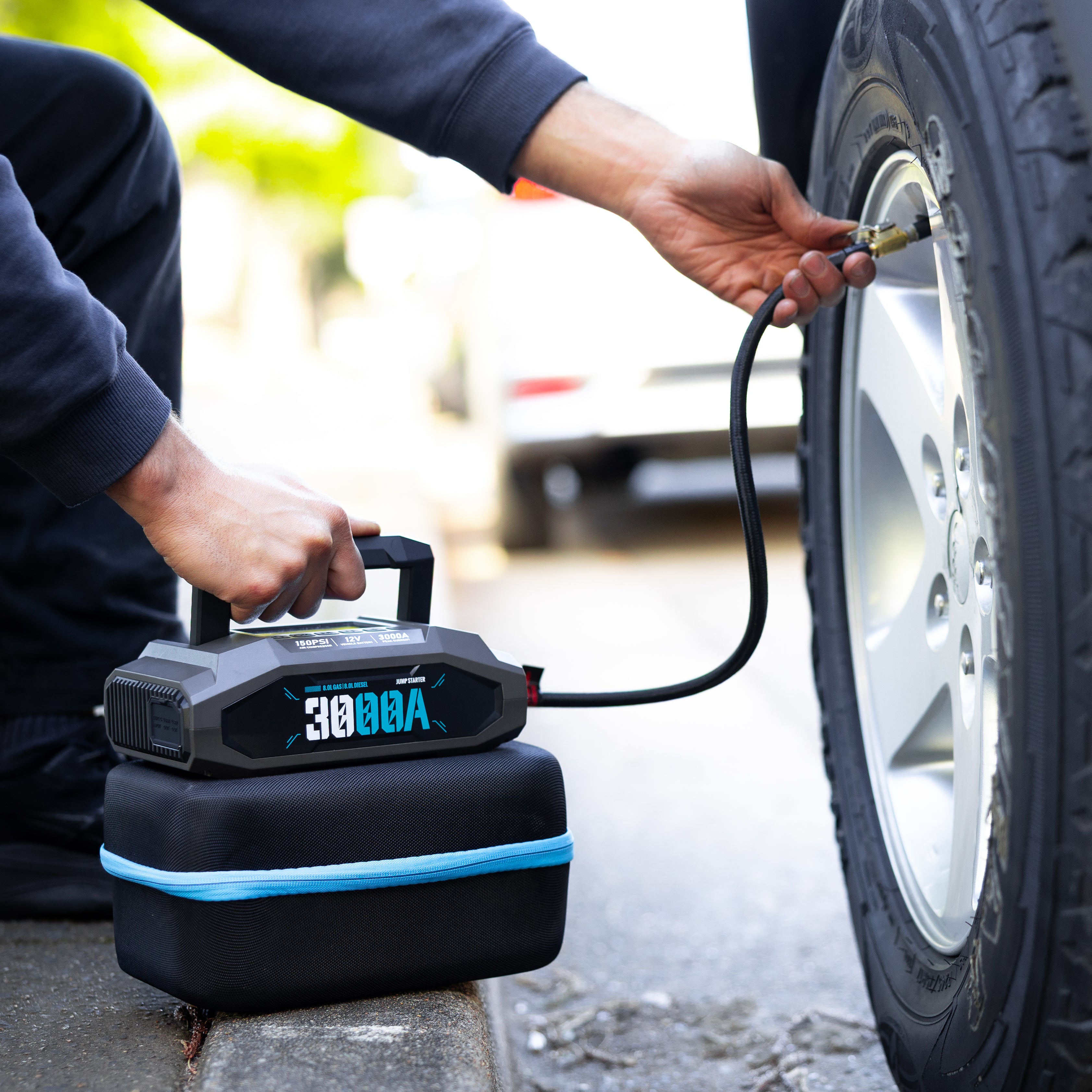 Person inflating a car tyre using the Boost N’ Inflate Pro, with the unit resting on its carry case beside the wheel. Shows real-world use of the jump starter and tyre inflator.