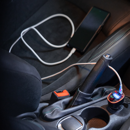 Bluetooth car charger plugged into a vehicle’s centre console, charging a smartphone with a white cable; My Garage Hero LED-lit charger shown in real in-car use.