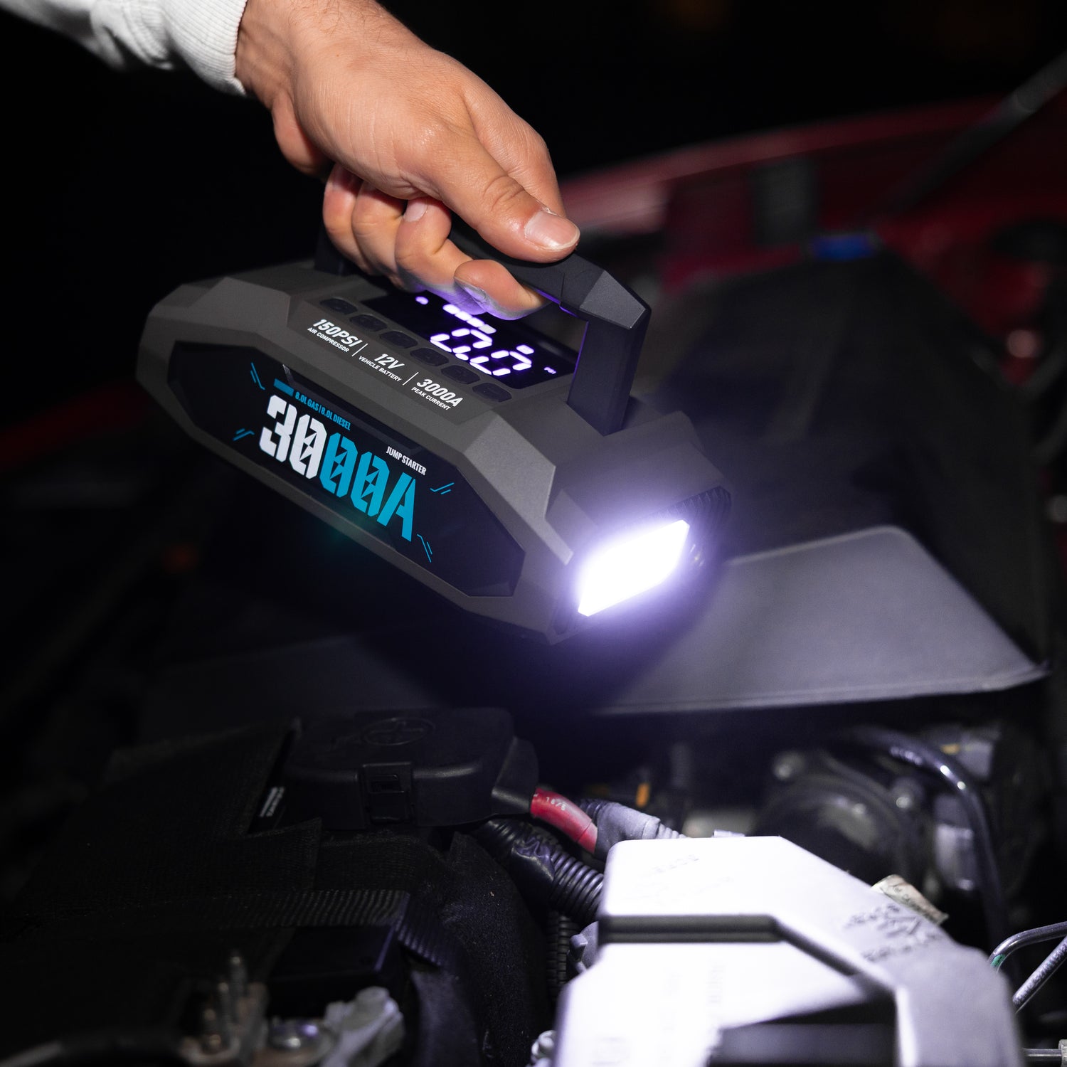 Multifunction jump starter & tire inflator being used to illuminate a car battery with a powerful torch. 