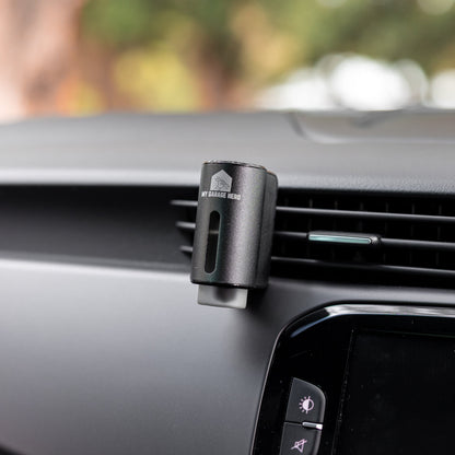 Car Diffuser – Premium Fragrance clipped to a vehicle air vent in a real in-car setting, showing the sleek black metal design against the dashboard with a blurred outdoor background.