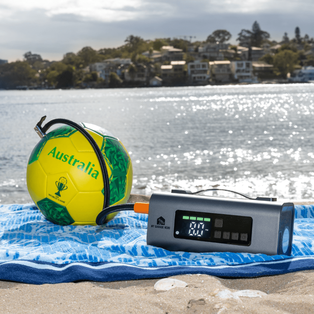 portable jump starter and air pump tyre inflator being used to inflate a soccer ball on a beach. 