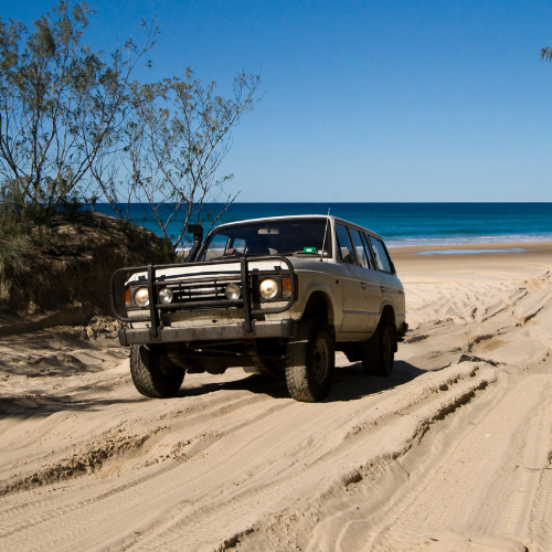 4x4 vehicle on a sandy beach with ocean and clear sky in the background