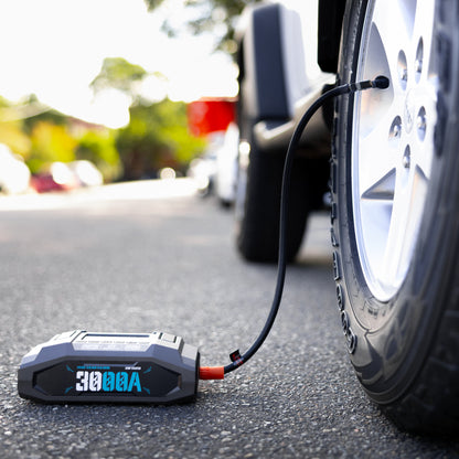 Boost N’ Inflate Pro by My Garage Hero inflating a car tyre on the side of the road, showing the 3000A jump starter and portable air compressor connected to the tyre valve.