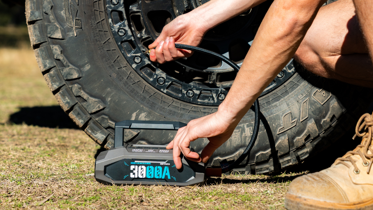 Person using a digital tire inflator and jump starter selecting its pressure on its digital display on a tire outdoors