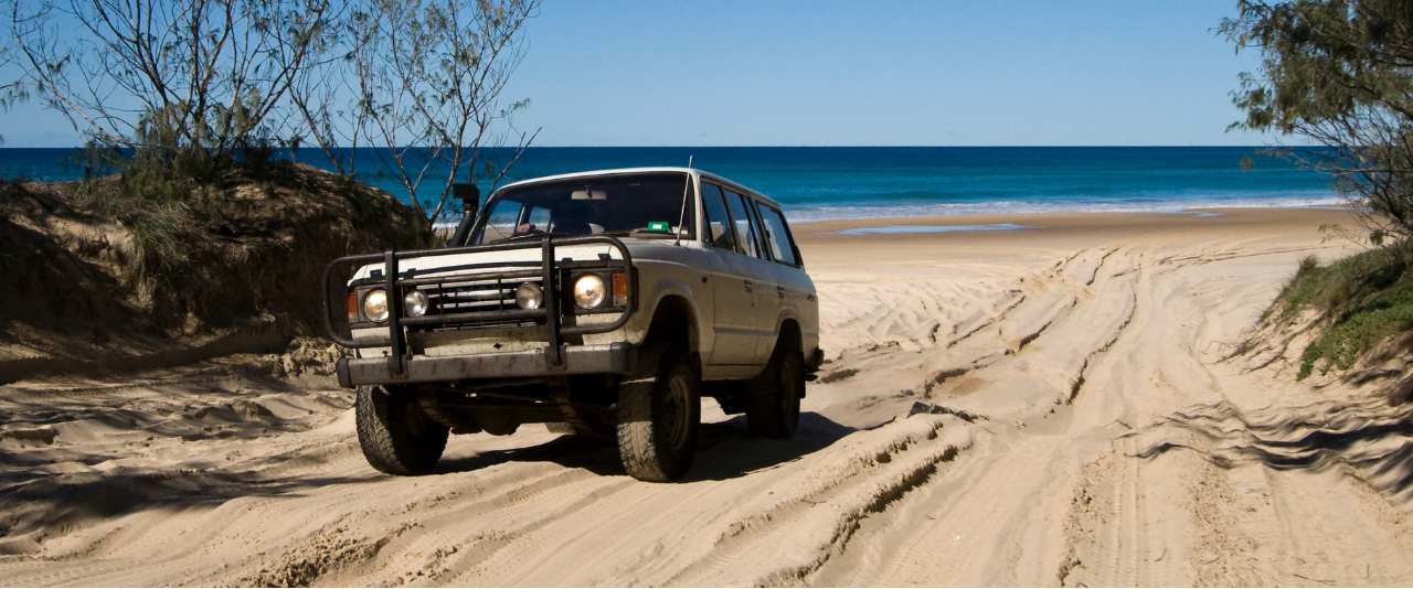 4WD driving on a sandy beach track with ocean in the background for vehicle education blog banner